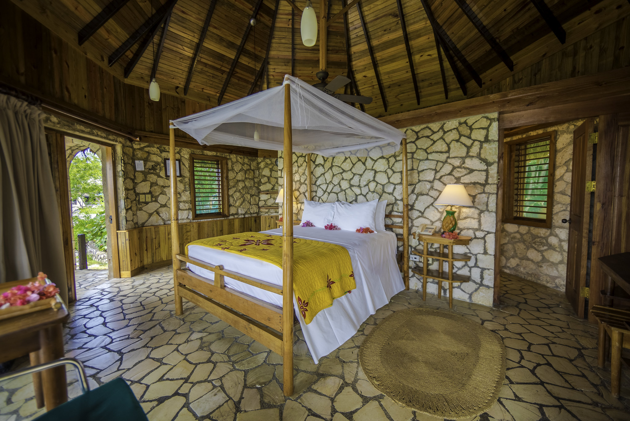 Rockhouse villa interior with four-poster bed under a thatched roof and stone walls